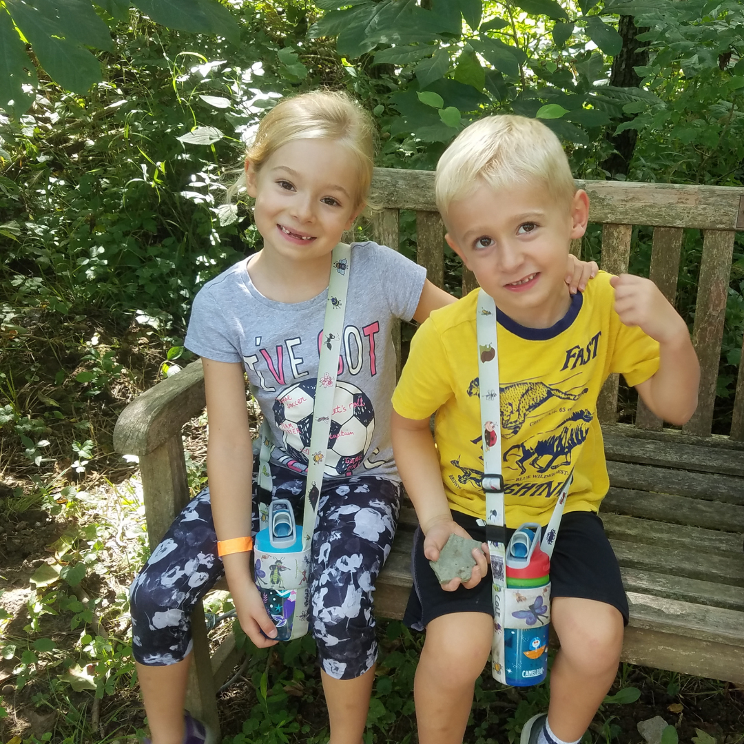 A young blonde girl and a young blonde boy sit on a bench at the Nature Center